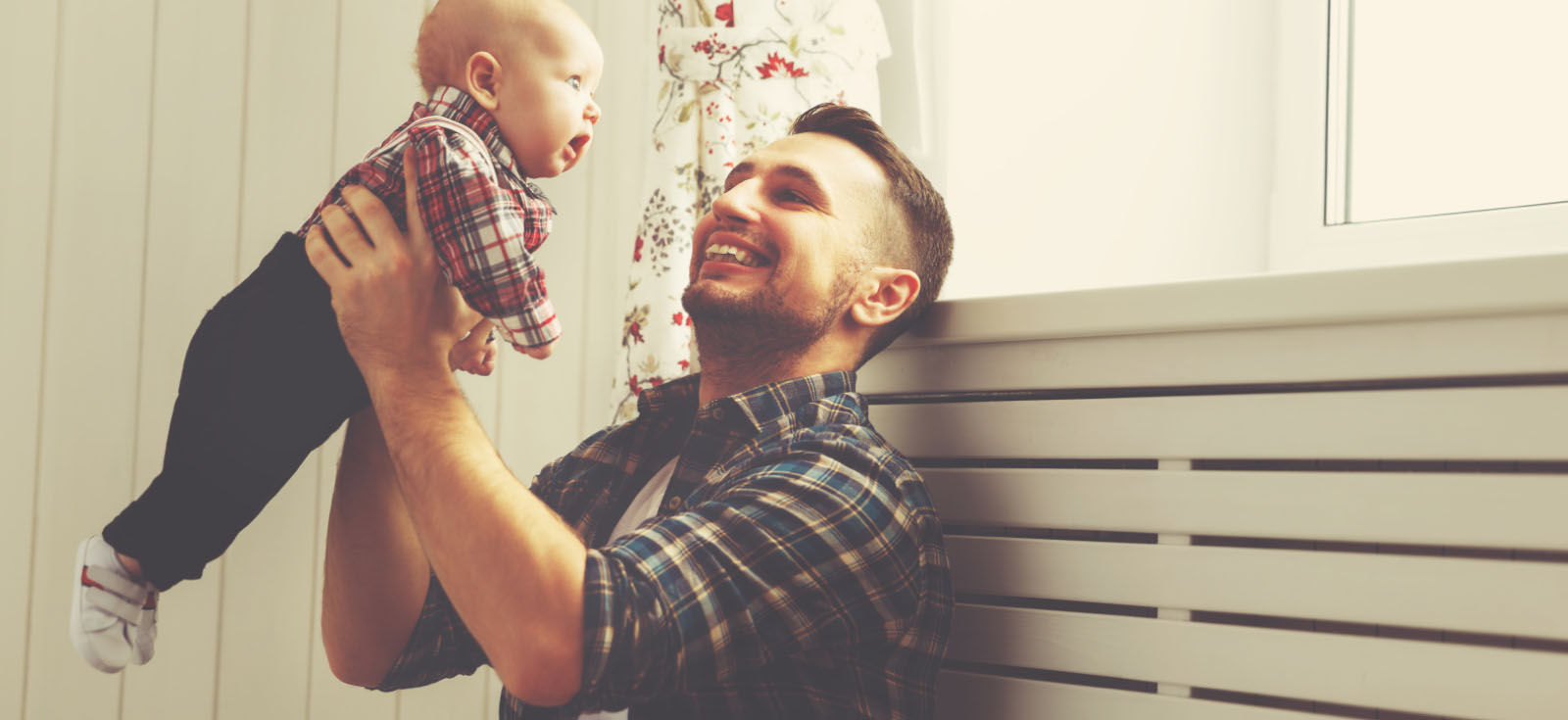 A man holding a baby up over his head to look out a window